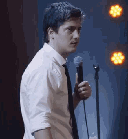 a man in a white shirt and black tie is holding a microphone on stage .