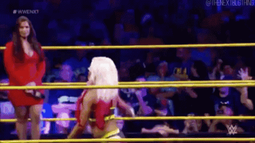 a woman in a red dress is standing in a wrestling ring with a woman in a red dress standing behind her .