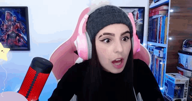 a woman wearing pink headphones and a knitted hat looks surprised