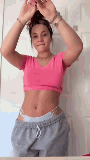 a woman in a pink crop top and grey sweatpants is standing in front of a door