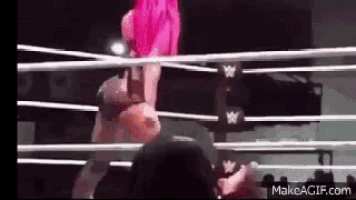 a woman with pink hair is standing in a wrestling ring with a crowd watching .