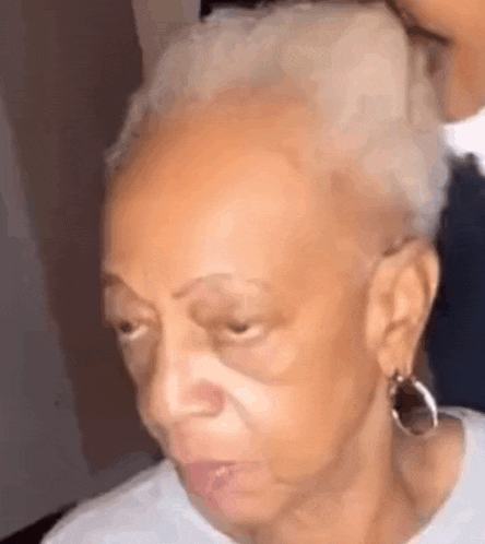 a close up of an elderly woman 's face with a bun in her hair and earrings .