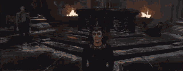 a woman in a black dress is standing in front of a statue with fire coming out of it .