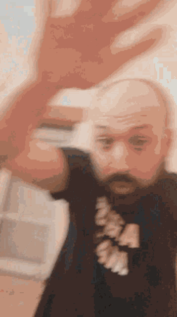 a bald man with a beard is making a funny face while holding his hand up in the air .