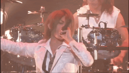 a man singing into a microphone with a drummer in the background