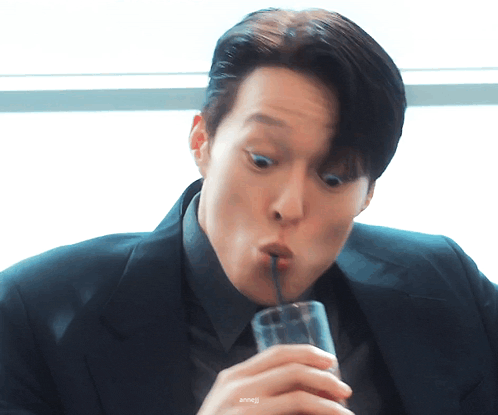 a man in a suit is drinking from a glass with a straw in his mouth