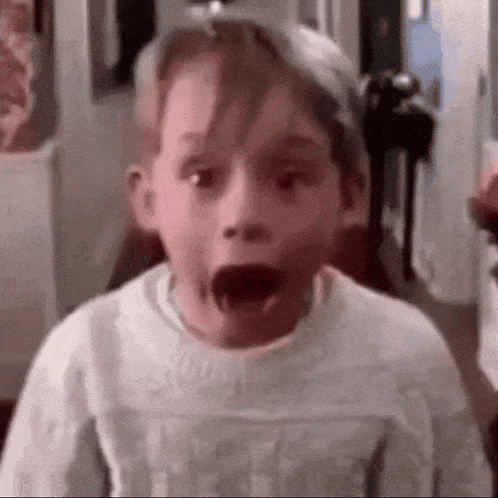 a young boy is making a surprised face while wearing a white sweater .