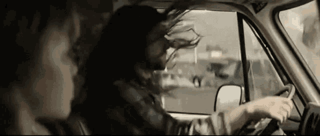 a man with long hair is driving a car with a woman sitting in the back seat .