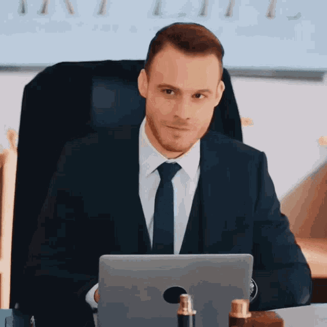 a man in a suit and tie is sitting at a desk with a laptop computer .