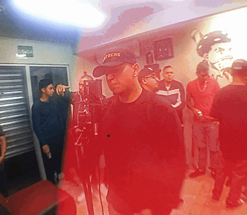 a man wearing a techs hat stands in a room with other people