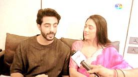 a man and woman are sitting on a couch being interviewed by a reporter