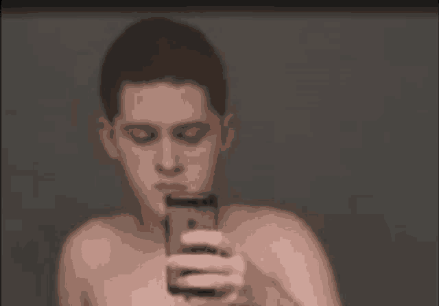 a shirtless man is taking a selfie with his cell phone .
