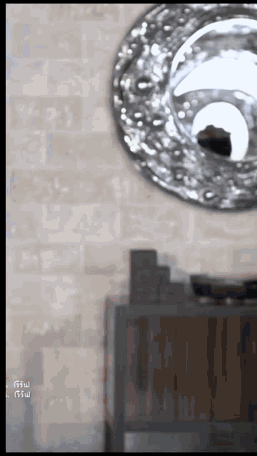 a round silver mirror hangs on a brick wall above a wooden table