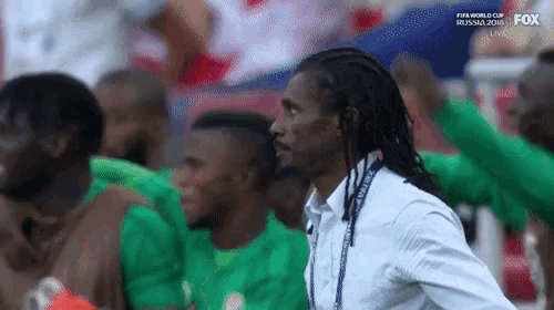 a man with dreadlocks is standing in front of a group of soccer players during a soccer game .
