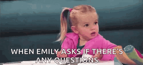 a little girl in a pink jacket is sitting at a table talking to someone .