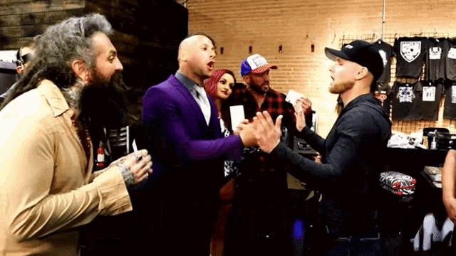 a group of men are standing in a room talking to each other . one of the men is wearing a purple suit .
