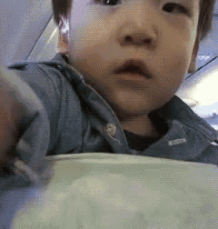 a baby in a blue shirt is sitting on a plane looking at the camera .