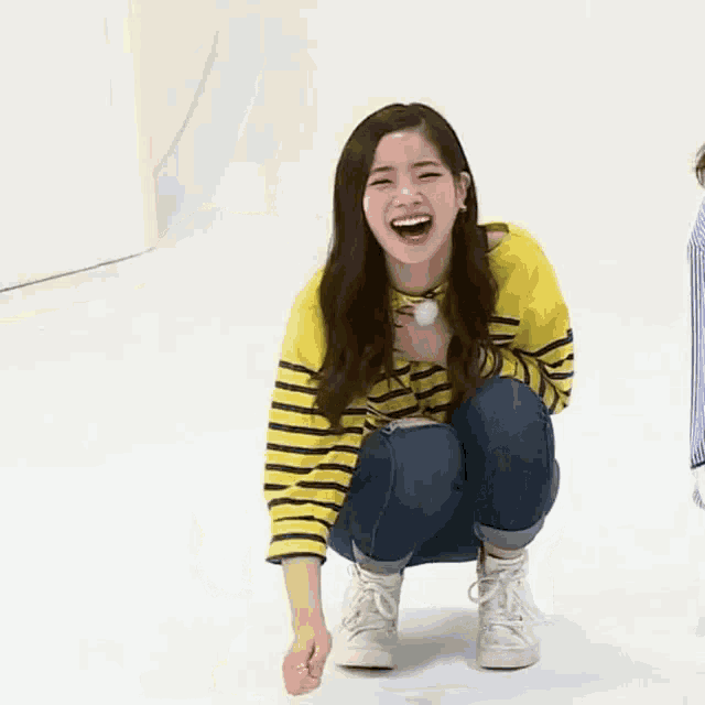 a woman in a yellow and black striped shirt is squatting on the floor .