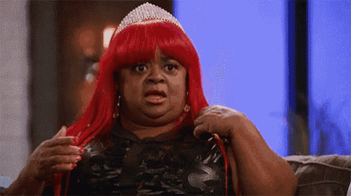 a woman in a red wig and tiara is sitting on a couch .