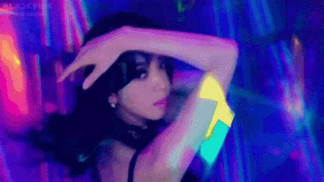 a woman is dancing in front of a colorful background in a dark room .