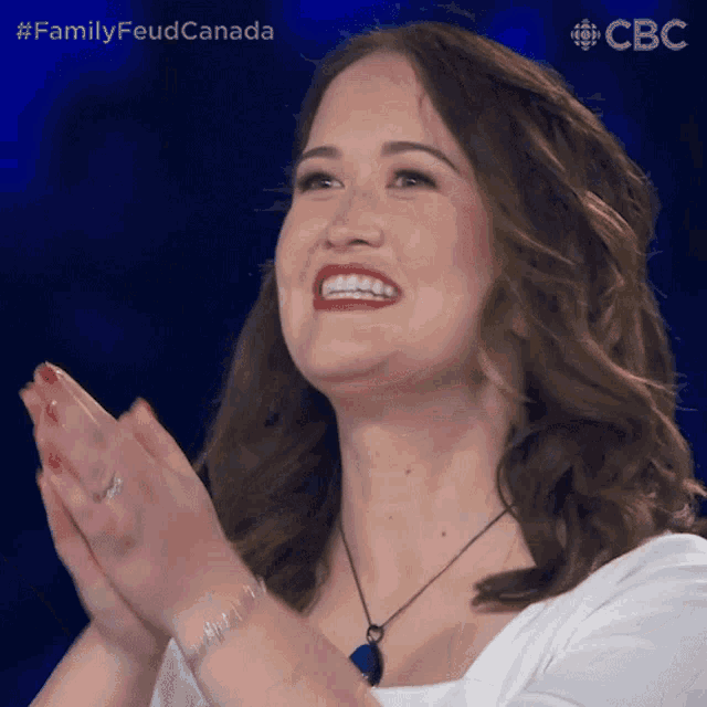 a woman is smiling and clapping her hands in front of a blue background that says familyfeud canada