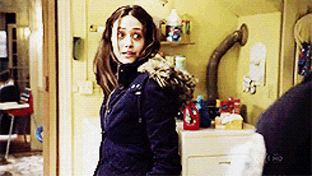 a woman in a blue jacket with a fur hood stands in a room
