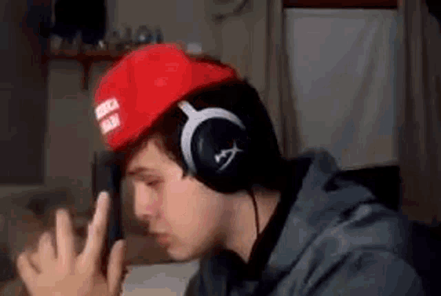 a man wearing headphones and a red hat is holding a cell phone .