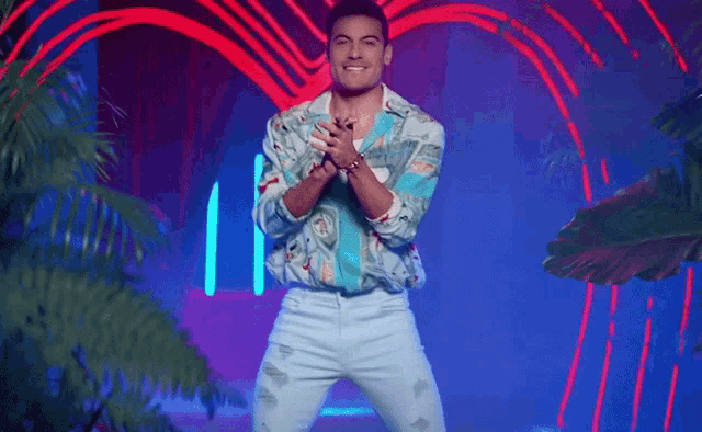 a man in a colorful shirt and blue jeans is dancing in front of a heart shaped neon sign .