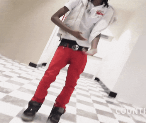 a man wearing red pants and a white shirt is standing on a checkered floor