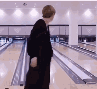 a man is walking down a bowling alley with a bowling ball in his hand .