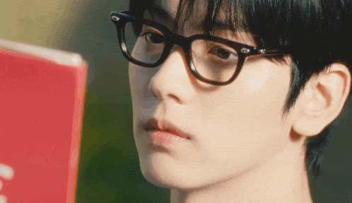 a close up of a person wearing glasses looking at a book