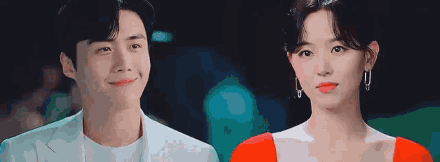 a man and a woman are standing next to each other and smiling . the woman is wearing a red dress .