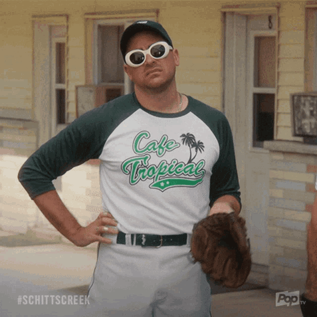 a man wearing sunglasses and a cafe tropical shirt holds a baseball glove