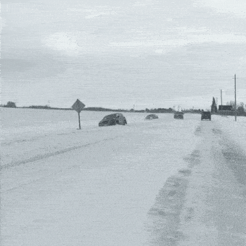 a black and white photo of a snowy road with a police car in the background