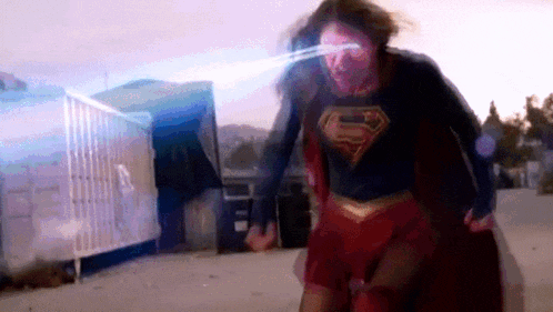 a woman in a superman costume is running with a laser beam coming out of her eyes .