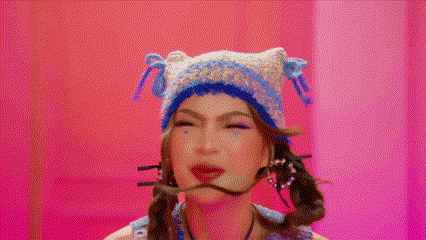a woman wearing a hat and tie is making a funny face in a pink room .