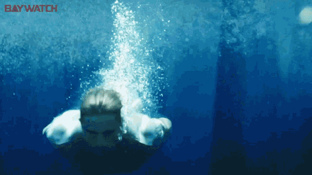 a man is swimming in the ocean with the word baywatch on the bottom right