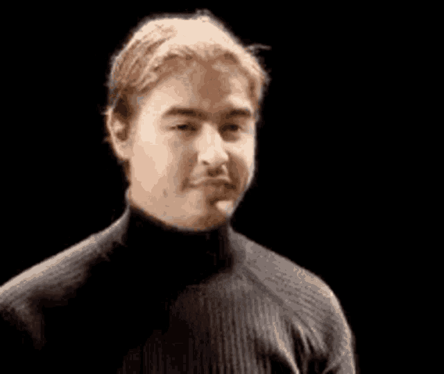 a man wearing a black turtleneck sweater is making a funny face in front of a black background .
