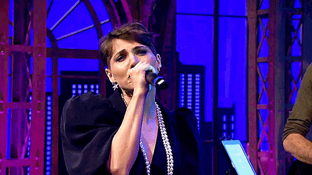 a woman singing into a microphone with a pearl necklace