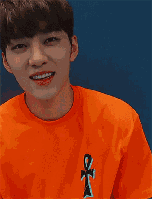 a young man wearing an orange shirt with an ankh on the front