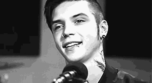 a young man with a tattoo on his neck is smiling in front of a microphone in a black and white photo .