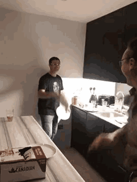 a man is standing in a kitchen holding a plate while another man stands behind him .