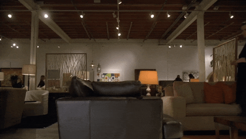 a man in a black coat walks through a living room filled with furniture and lamps