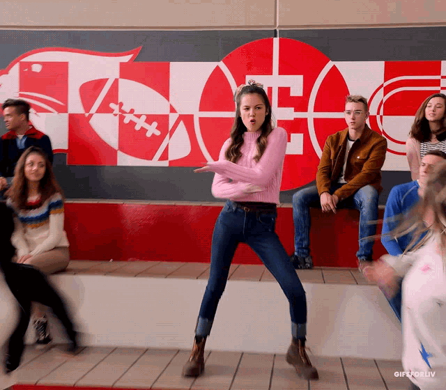 a girl in a pink sweater is dancing in front of a wall with a football and a t on it
