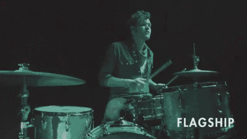 a man is playing drums in a dark room with the word flagship above him