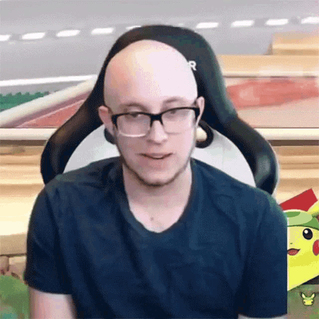 a bald man wearing glasses is sitting in a black chair