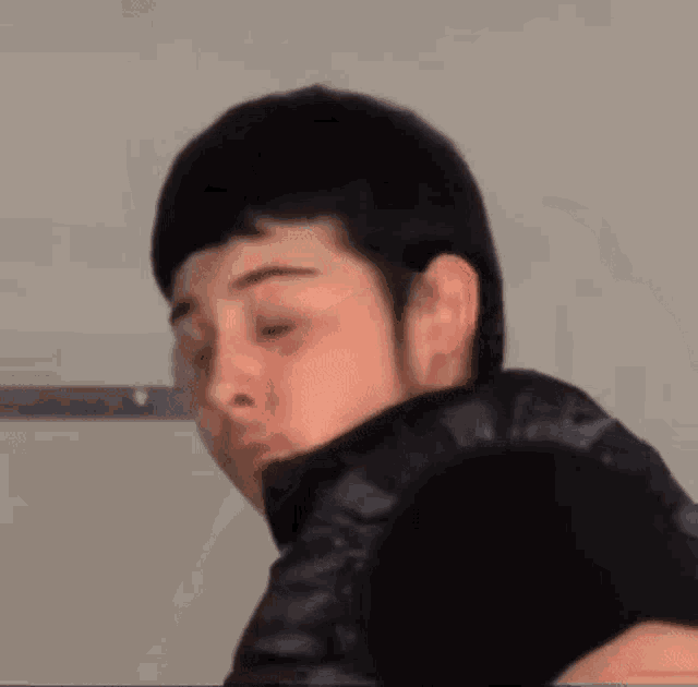 a young man in a black jacket is making a funny face and looking at the camera .