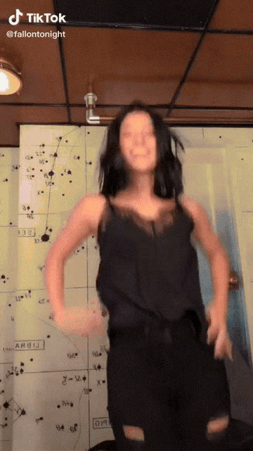 a woman in a black tank top is dancing in front of a wall with a map on it that says dm