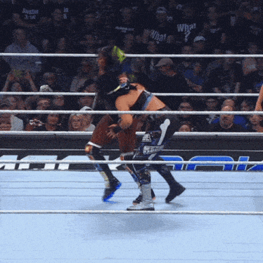 two wrestlers in a ring with one wearing a t-shirt that says what on it