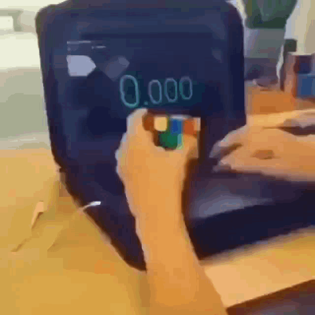 a person is holding a rubik 's cube in front of a screen that says 0.0000 on it